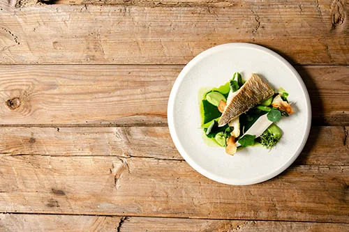 A plate of fish and vegetables on a wooden table.