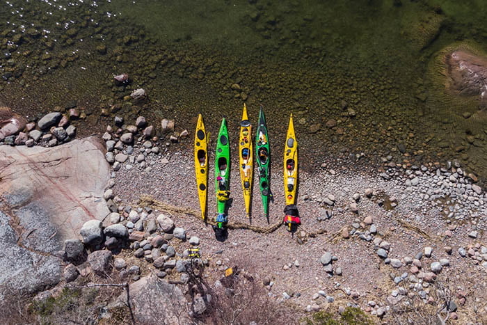 A group of colourful kayaks on a rocky shore.